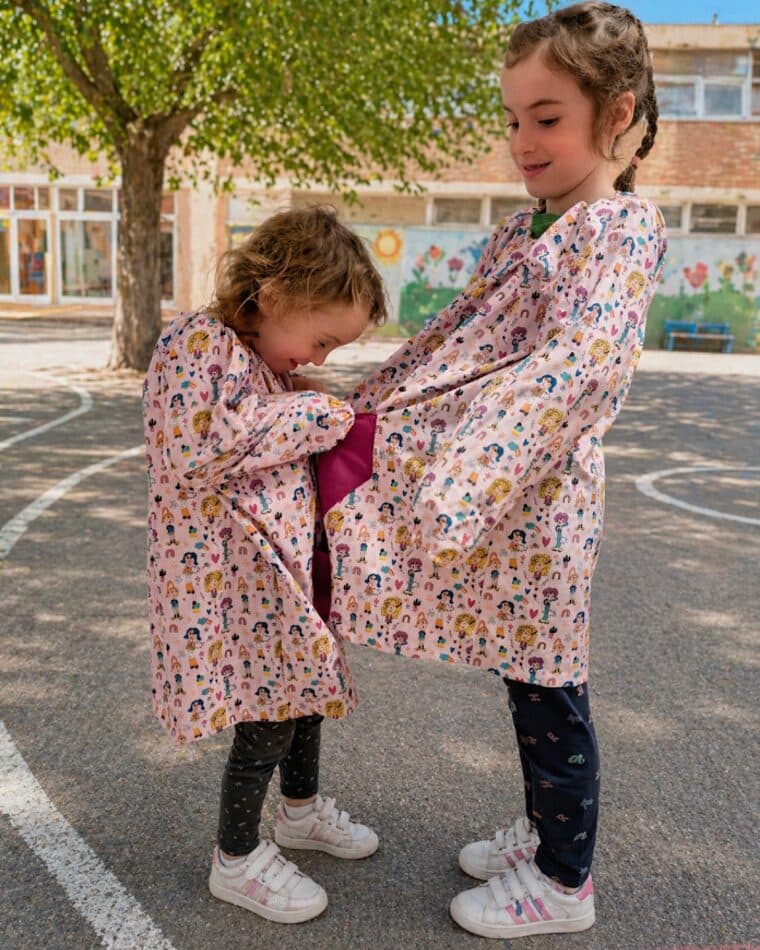 Dos niñas con bata escolar de estampado floral en el patio