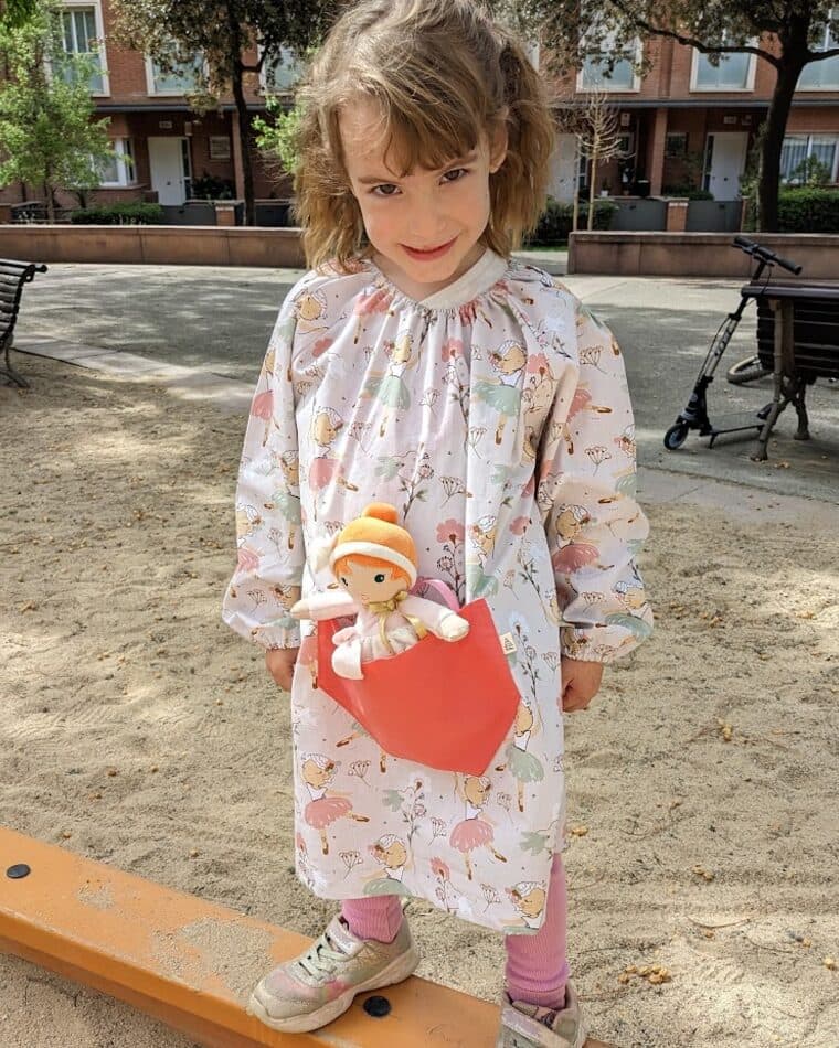 Niña con bata de estampado floral y bolsillo naranja con un muñeco
