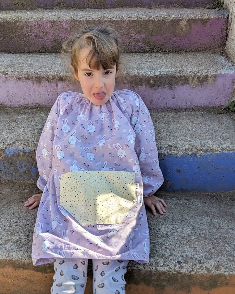 Niña con bata de estampado suave y bolsillo amarillo en unas escaleras