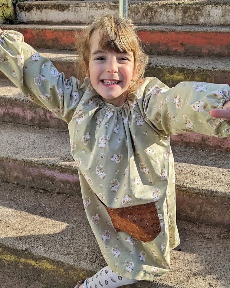 Niña con bata verde con los brazos abiertos