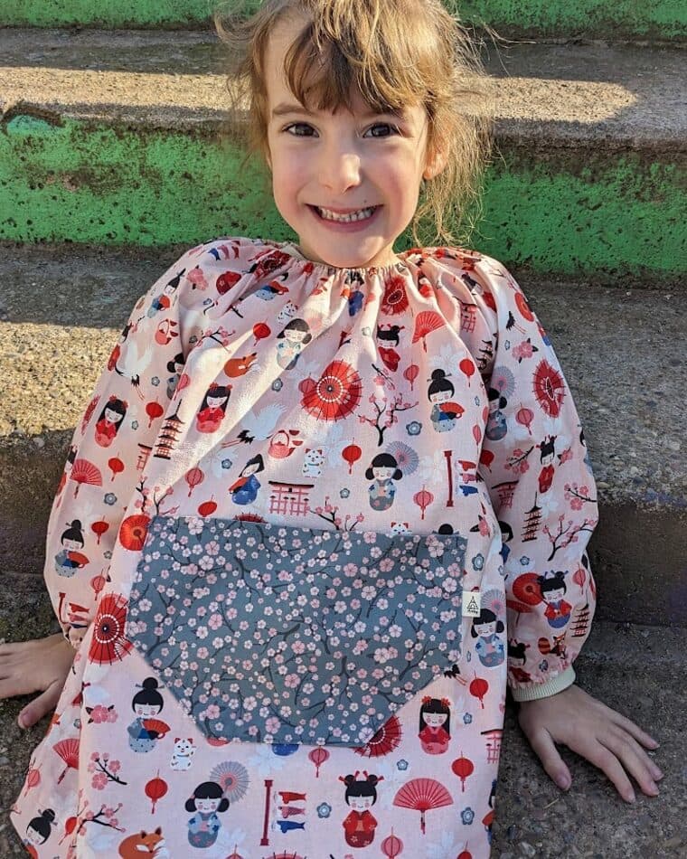 Niña sonriente con bata de estampado de muñecos y bolsillo azul