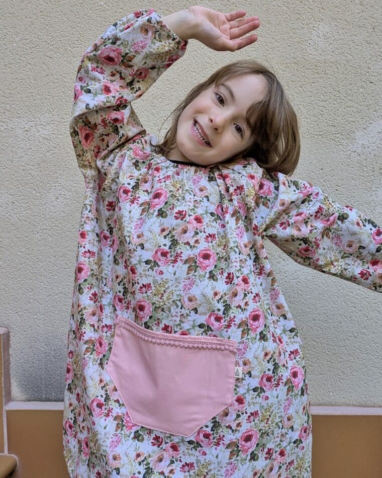 Niña con bata floral y bolsillo rosa con el brazo en alto