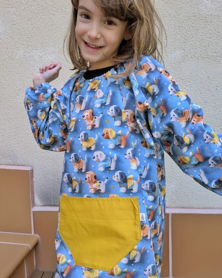 Niña con bata azul de animales y bolsillo amarillo