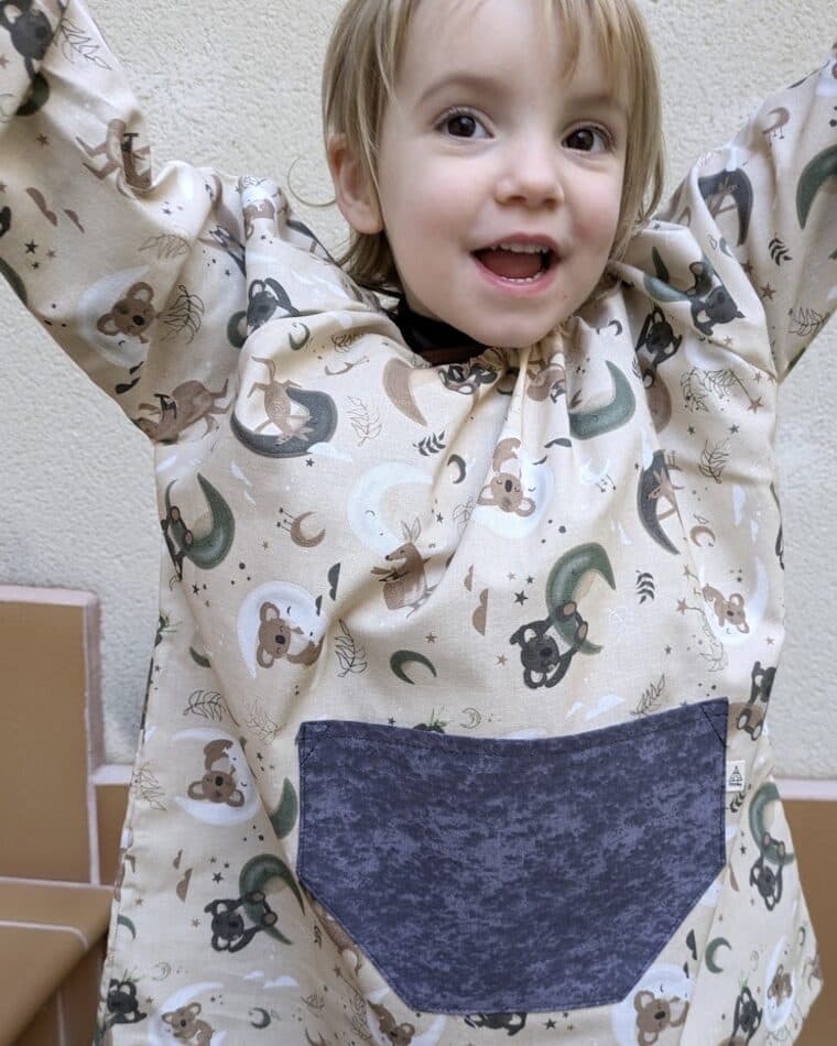 Niña pequeña con bata de estampado de arcoíris y bolsillo gris