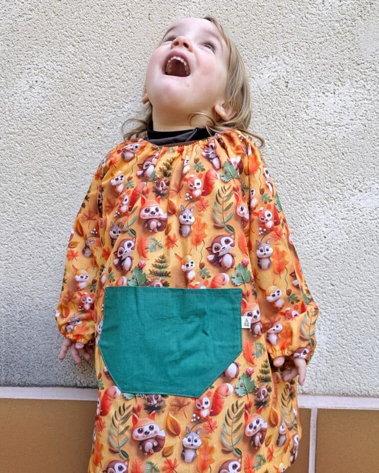 Niño riendo con bata de estampado de pájaros y bolsillo turquesa