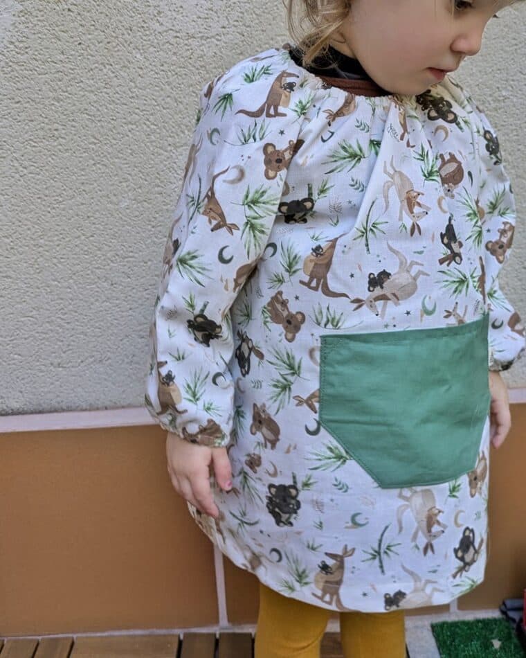 Niña con bata de estampado de animales y bolsillo verde