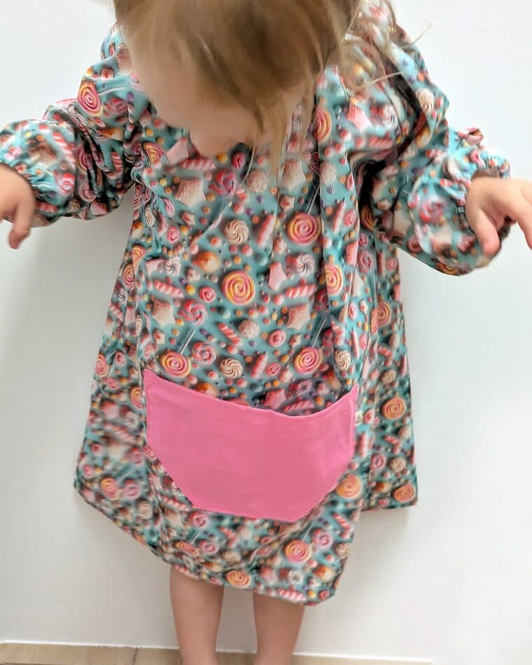 Niña pequeña con bata de flores rojas y bolsillo rosa