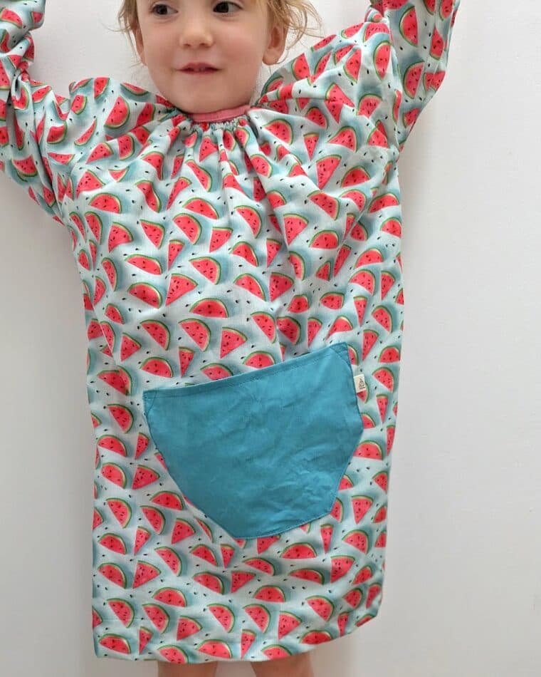Niña con bata de estampado rojo y bolsillo turquesa