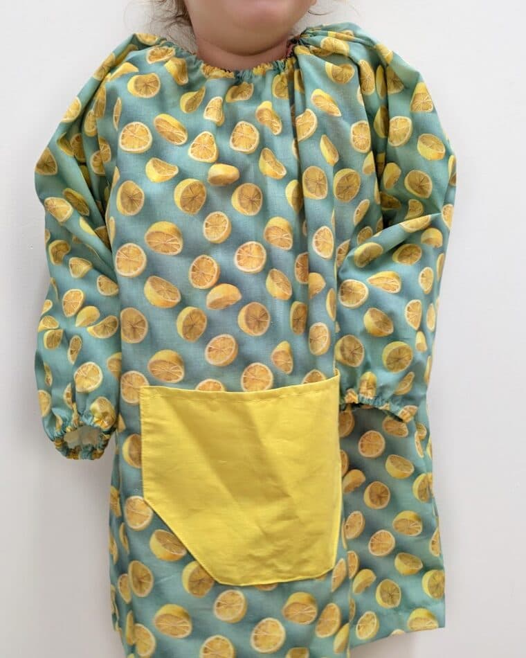 Niña con bata verde de topos y bolsillo amarillo