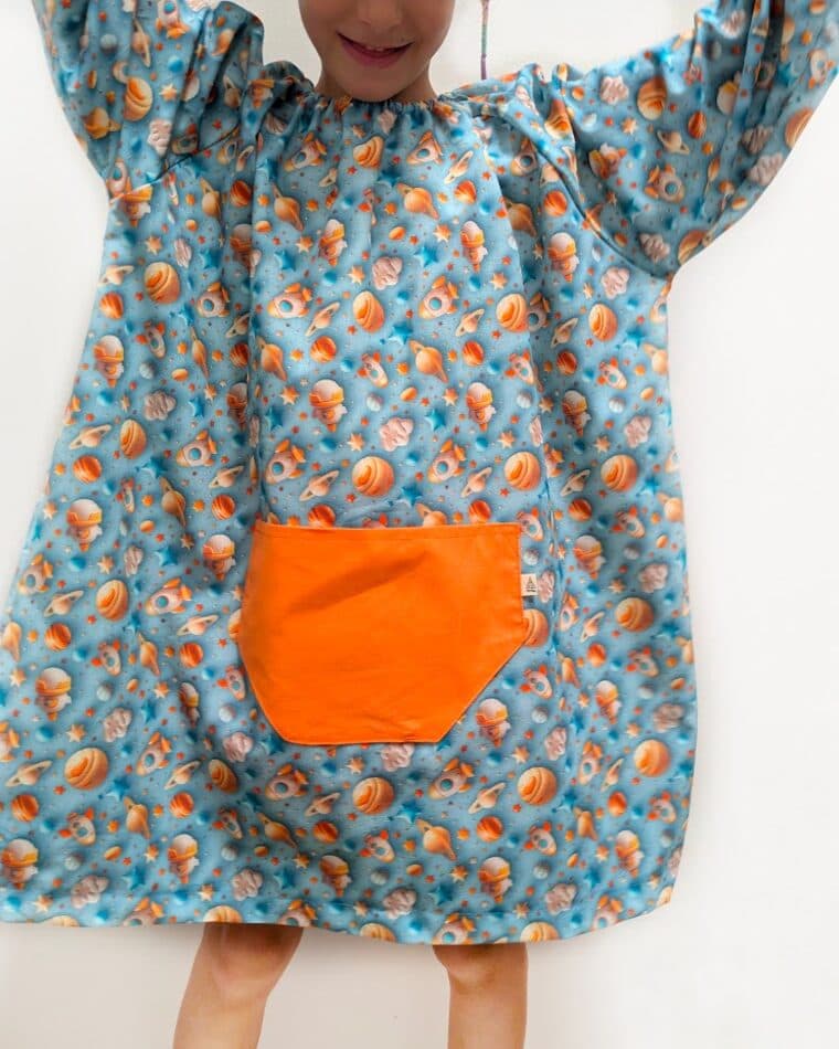Niña con bata de estampado azul y bolsillo naranja