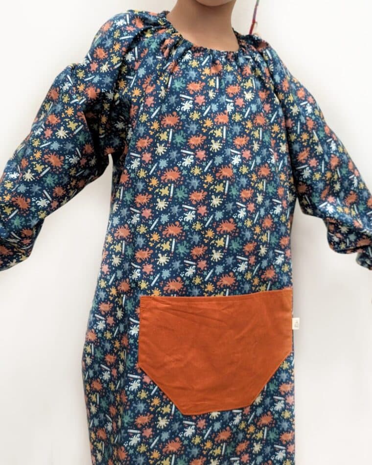Niña con bata de estampado turquesa y bolsillo naranja