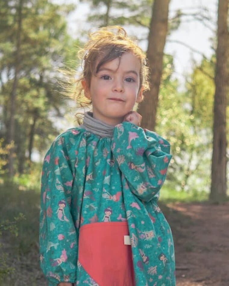 Niña con bata verde estampada y bolsillo rojo en un bosque