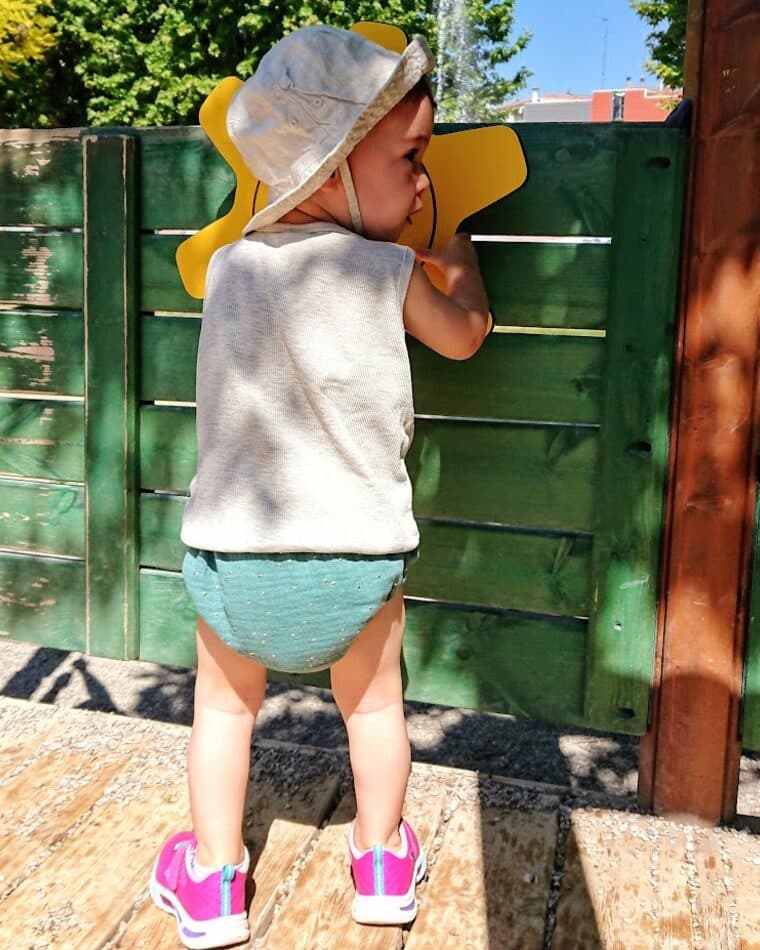 Bebé de espaldas con cubrepañal color agua y gorro amarillo
