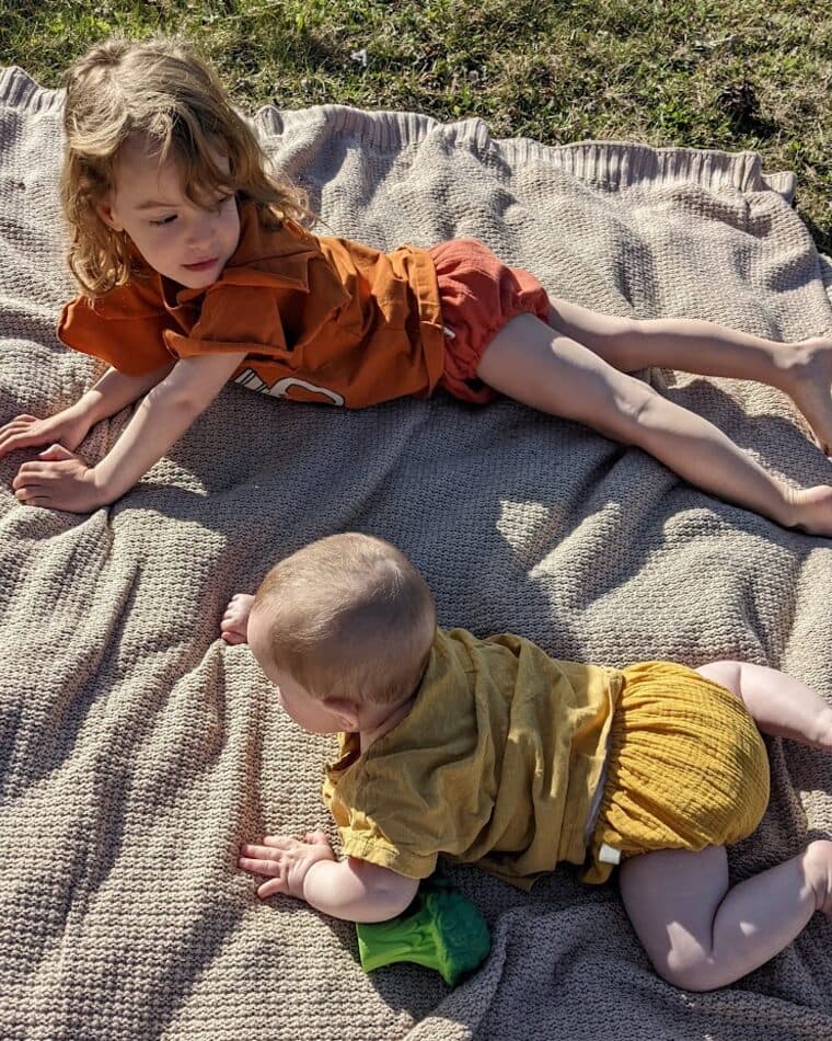 Dos niños con cubrepañales color teja y mostaza en el jardín