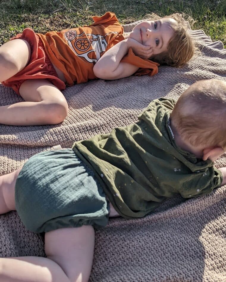 Dos niños con cubrepañales color teja y verde sobre una manta